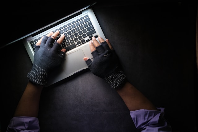 Someone typing on a Macbook wearing gloves. It looks shady.