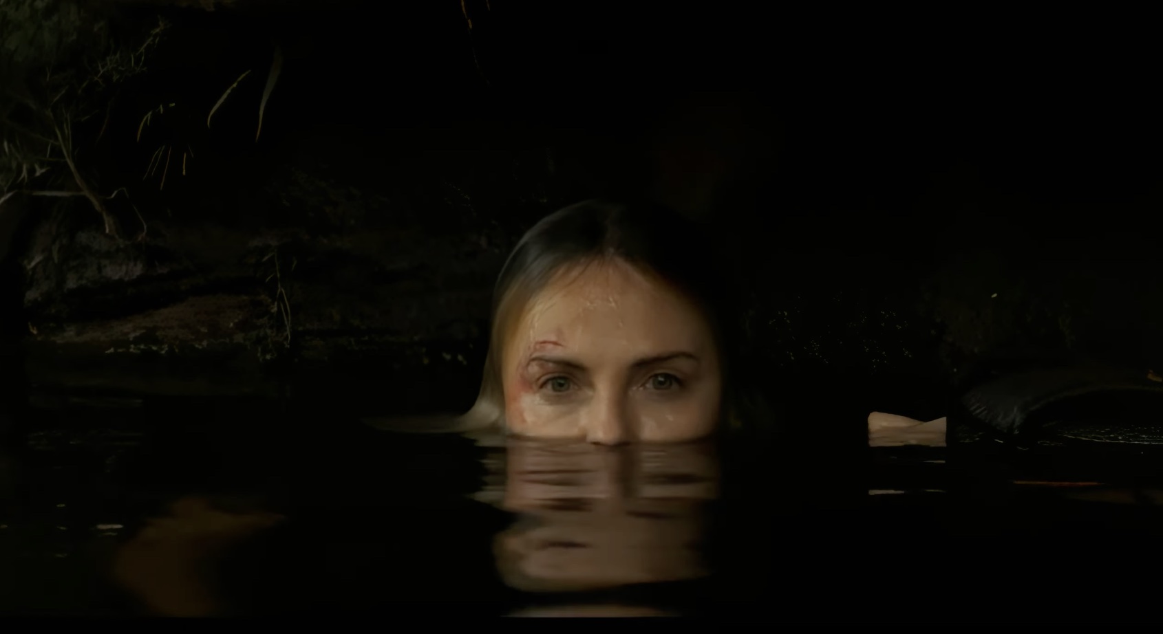 Charlize Theron in Apex. Ze ligt in het water. Haar ogen zijn alleen boven water.