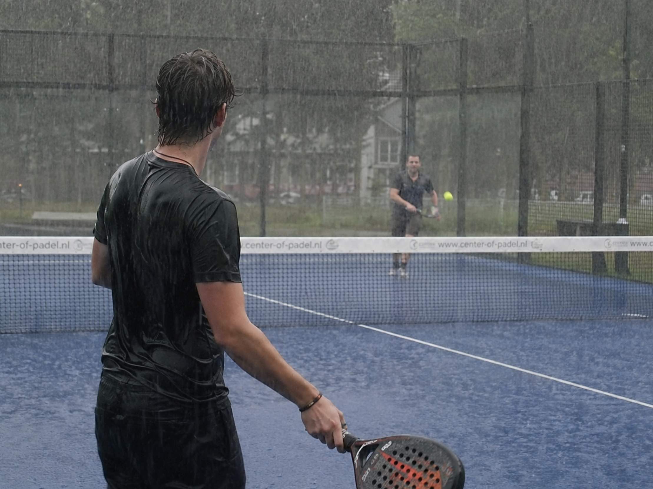 Twee mannen spelen een potje padel in de regen