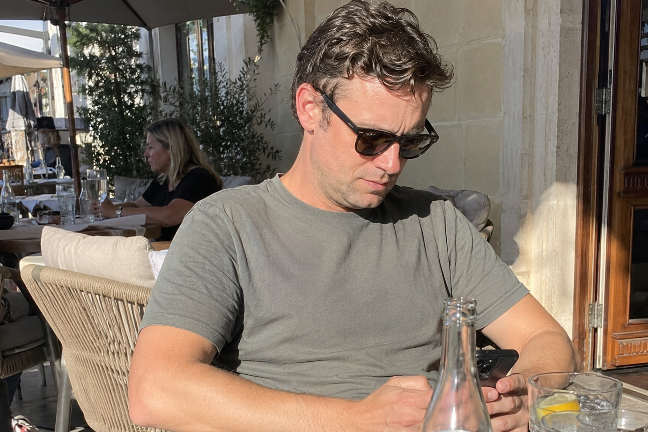 Man in de zon kijkt op een terras naar zijn smartphone.