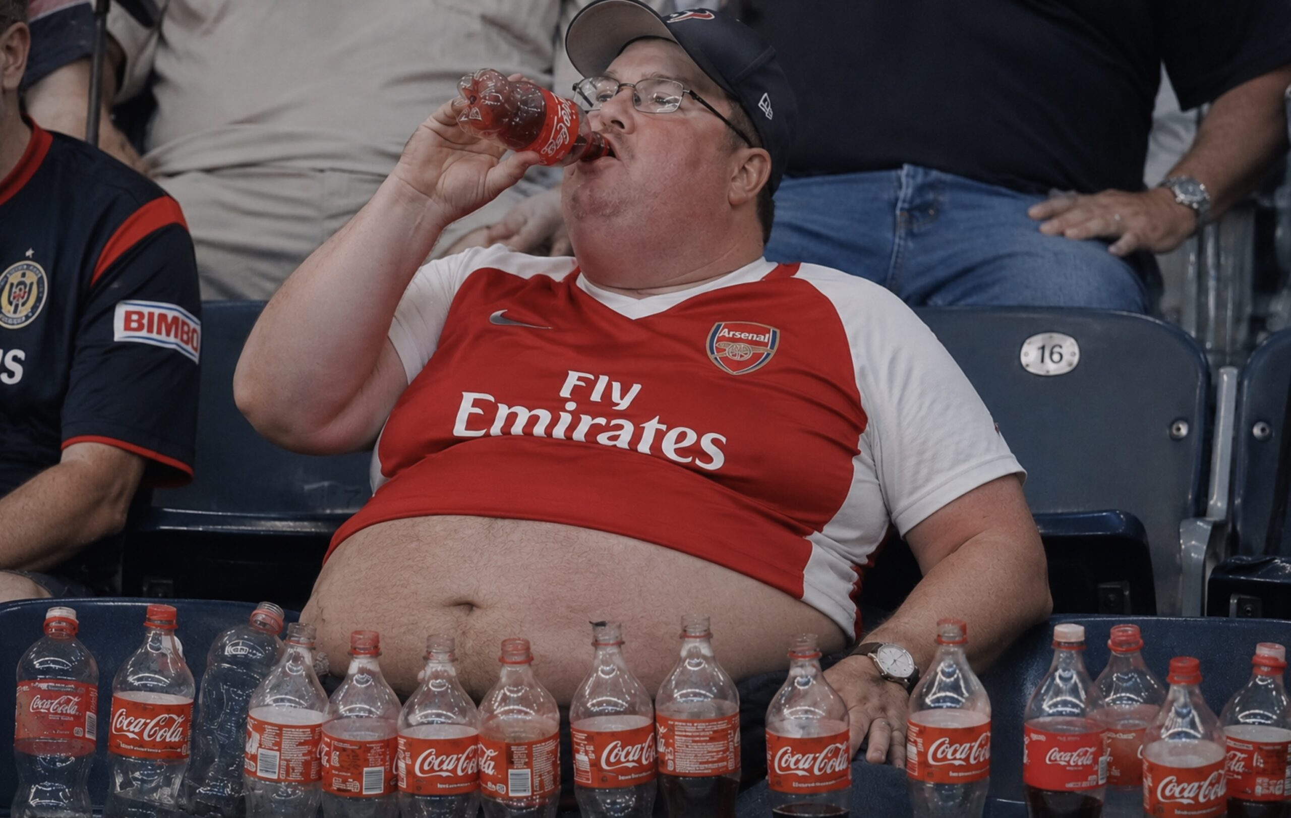 Een corpulente Amerikaan drinkt coca-coal. Hij heeft een Arsenal-shirt aan