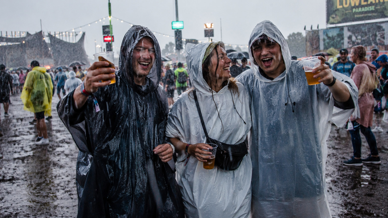 Drie mensen in de stromende regen op Lowlands met een poncho aan.